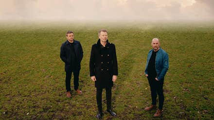 3 men standing slightly apart on grass with misty background