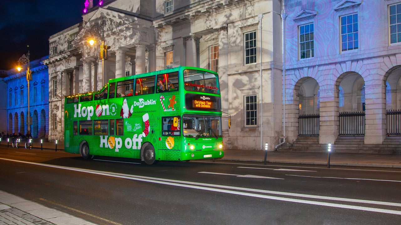 A green double decker bus at night outside old city buildings