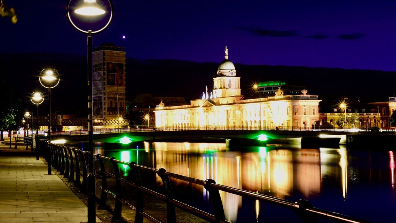 Riverside walkway at night with a building lit up in the background