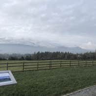 Wooden fence through a green field with snow capped mountains in the background