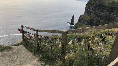 Sandy path leading to the sea with a wooden rail greenery and cliffs to the right