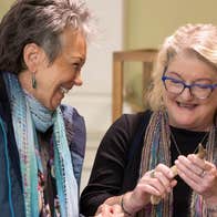 2 laughing women, one holding an artefact with display cases behind.