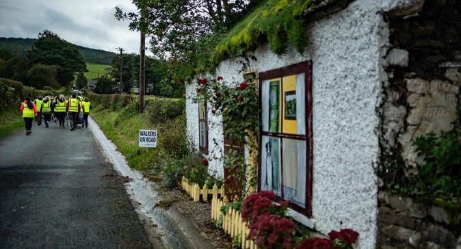 Looking down a country lane with group in hi-vis jackets walking away and old cottage in the foreground.