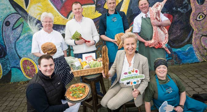 A group of smiling people each holding either food produce or small hashtag signs