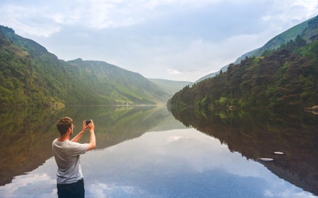 A man takes a photo across a lake and valley using a camera