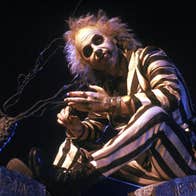 Beetlejuice is sitting by a tree, looking up at something.