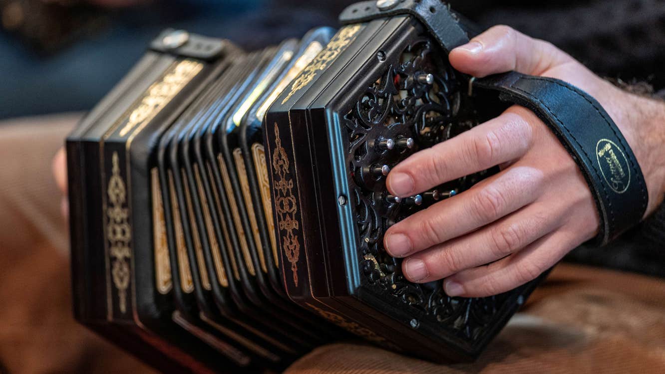 Close up view of pair of hands holding a small, black concertina.