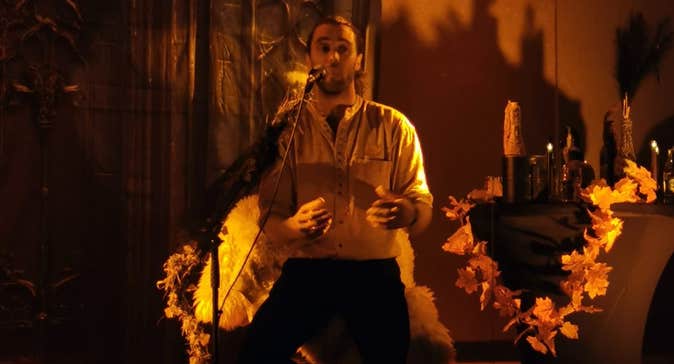 Man on stage singing/talking in candlelit lighting
