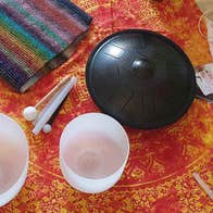 White, opaque glass bowls on a red and gold table cloth with small gongs and a stripy knitted piece of cloth.