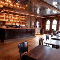 Interior of a traditional pub featuring a wooden bar with exposed brick walls and large arched windows
