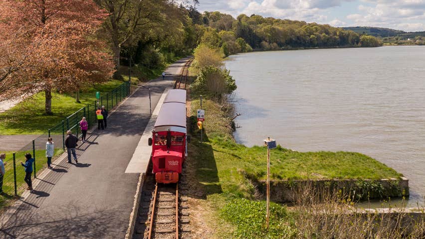 Train travelling along the Waterford Suir Valley Railway line with water beside it
