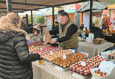 Person behind a stall with trays of little cakes handing a brown bag over to a lady