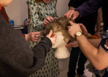 People looking at and touching a wig on a tour of a theatre