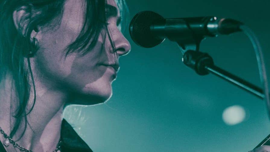 Close up side view of woman in front of a mic on a stand, playing a guitar.