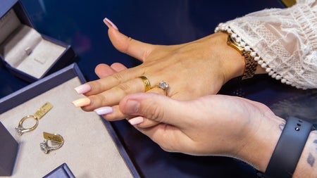 A close up of rings on fingers with a selection of rings on a counter