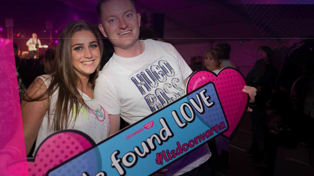 2 smiling people holding pink, large hearts and a hashtag sign.