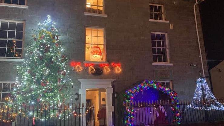 The front view of large, Georgian style building lit up at christmas with large tree.