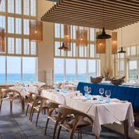 Bright coastal restaurant interior with sea views white clothed tables and blue seating
