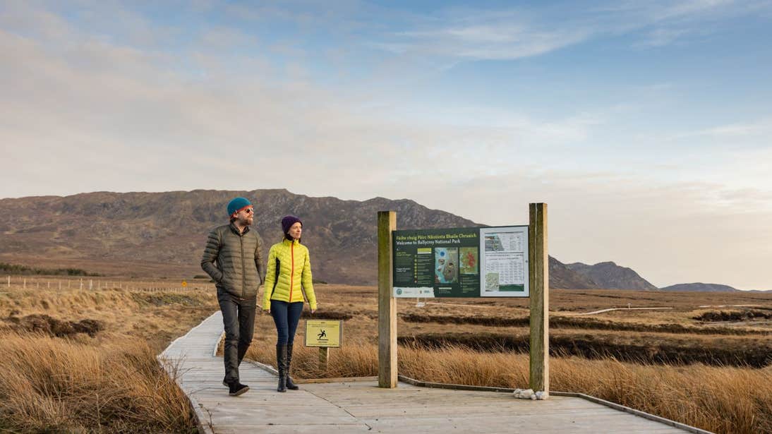 A couple walking on a boardwalk towards a sign in Wild Nephin Ballycroy, Co. Mayo