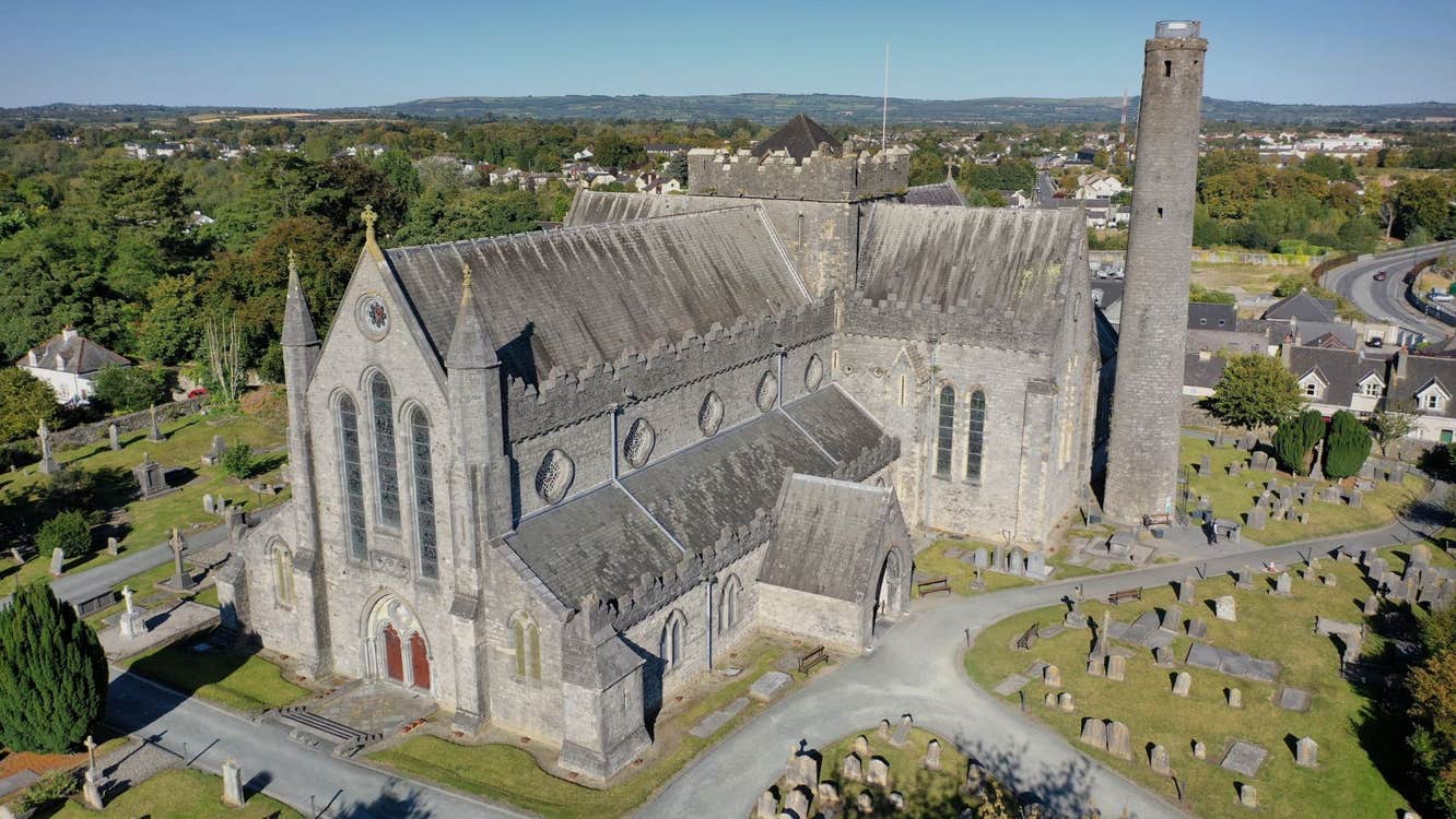 An aerial view of a cathedral building with a round tower beside it surrounded by grave stones