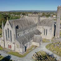 An aerial view of a cathedral building with a round tower beside it surrounded by grave stones