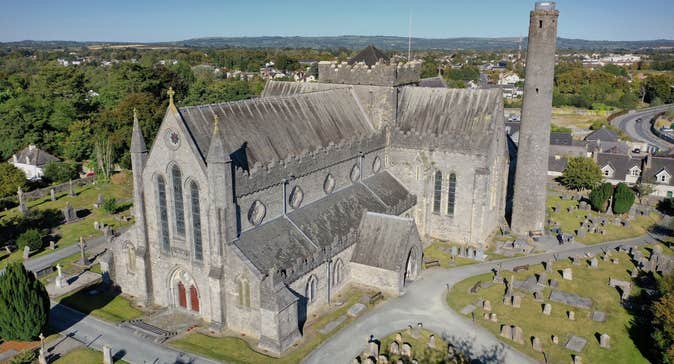 An aerial view of a cathedral building with a round tower beside it surrounded by grave stones