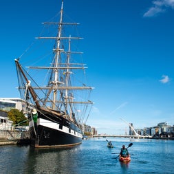 Two kayaks on the River Liffey paddling alongside a tall sailing ship