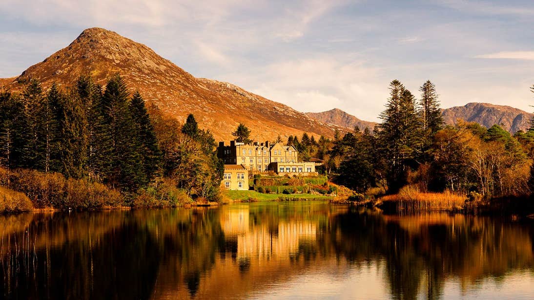 Ballynahinch Castle overlooking a lake with mountains and trees in the background