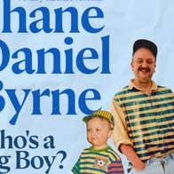 A smiling man in a stripy top standing with a young boy also in a stripy top, both with their hands in the shorts pockets.