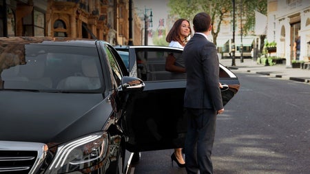 Person holding a car door as another person exits the car on a street