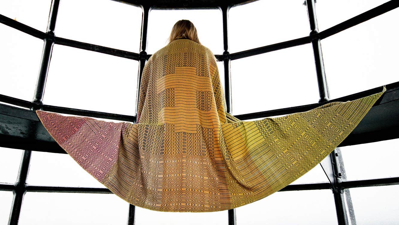 Person modelling a colourful scarf that is spread out over a bench