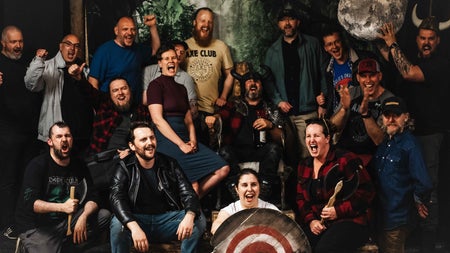 Group of smiling people holding axes and standing behind a target board
