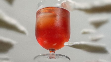 Looking up at an orange coloured cocktail in a short glass from beneath a glass surface