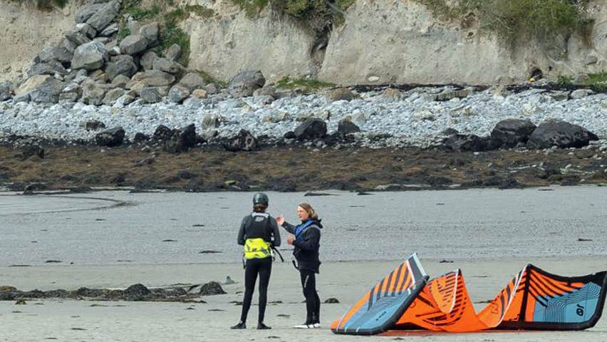 Two people on beach with orange and blue kite next to them