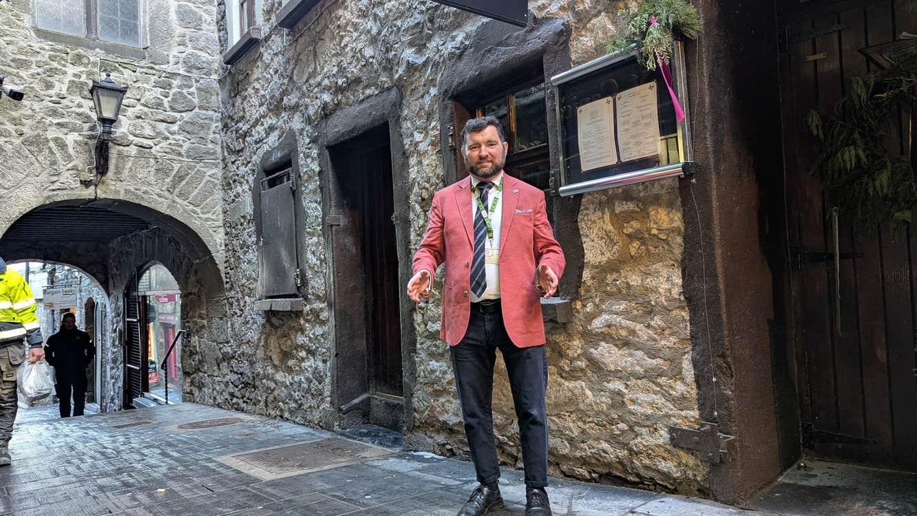 A tour guide in a pink jacket stands in a medieval laneway