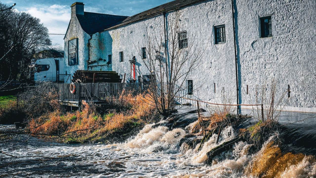 Historic whitewashed distillery buildings standing beside a flowing river