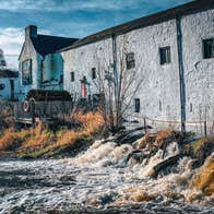 Historic whitewashed distillery buildings standing beside a flowing river