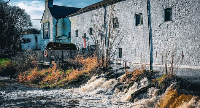 Historic whitewashed distillery buildings standing beside a flowing river