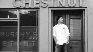Black and white image of the exterior of the restaurant with the chef standing in the doorway