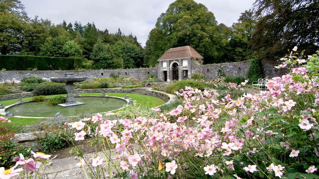 Fountain at Heywood Gardens in County Laois surrounded by a stone wall and pink flowers.