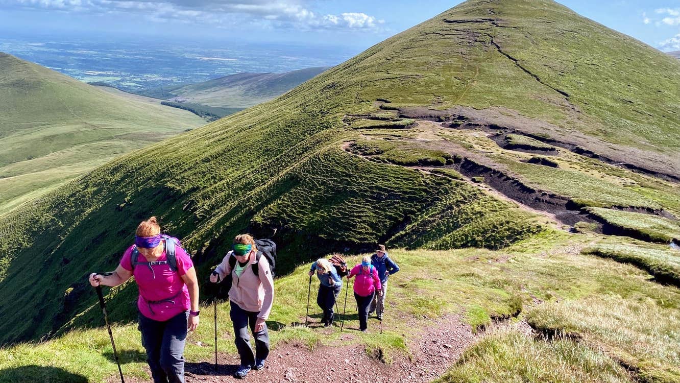 A group of hikers walking up a mountain path with another mountain in the background