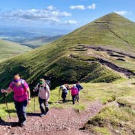 A group of hikers walking up a mountain path with another mountain in the background