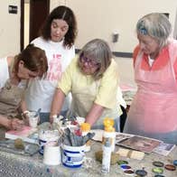 People in protective aprons and a teacher gathered around a table with art supplies