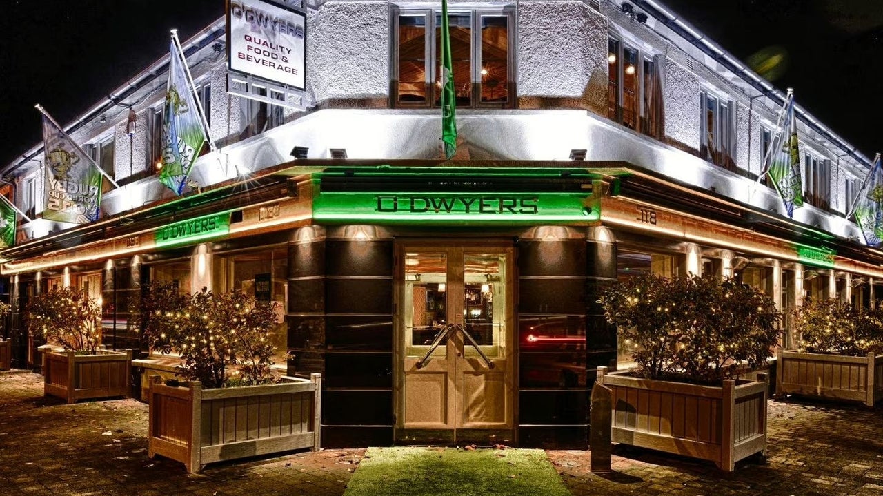 Outside a pub on a corner at night with the name on a green background and planters either side