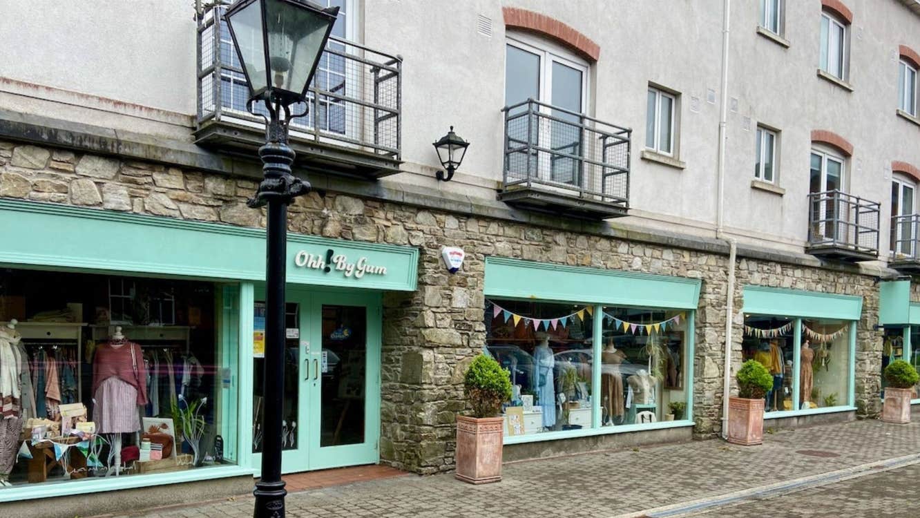 Shop front with mint green window and door frames and planters in front and a black lamp post on the street