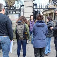A small tour group listening to a guide standing in front of black ornate railings