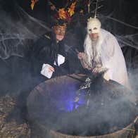 two people, one in white and one in black over a cauldron mixing it up
