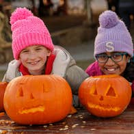 Two children beam with pride beside their freshly carved pumpkins at Nore Valley Park's Pumpkin Patch, a fun family activity included in every visit.
