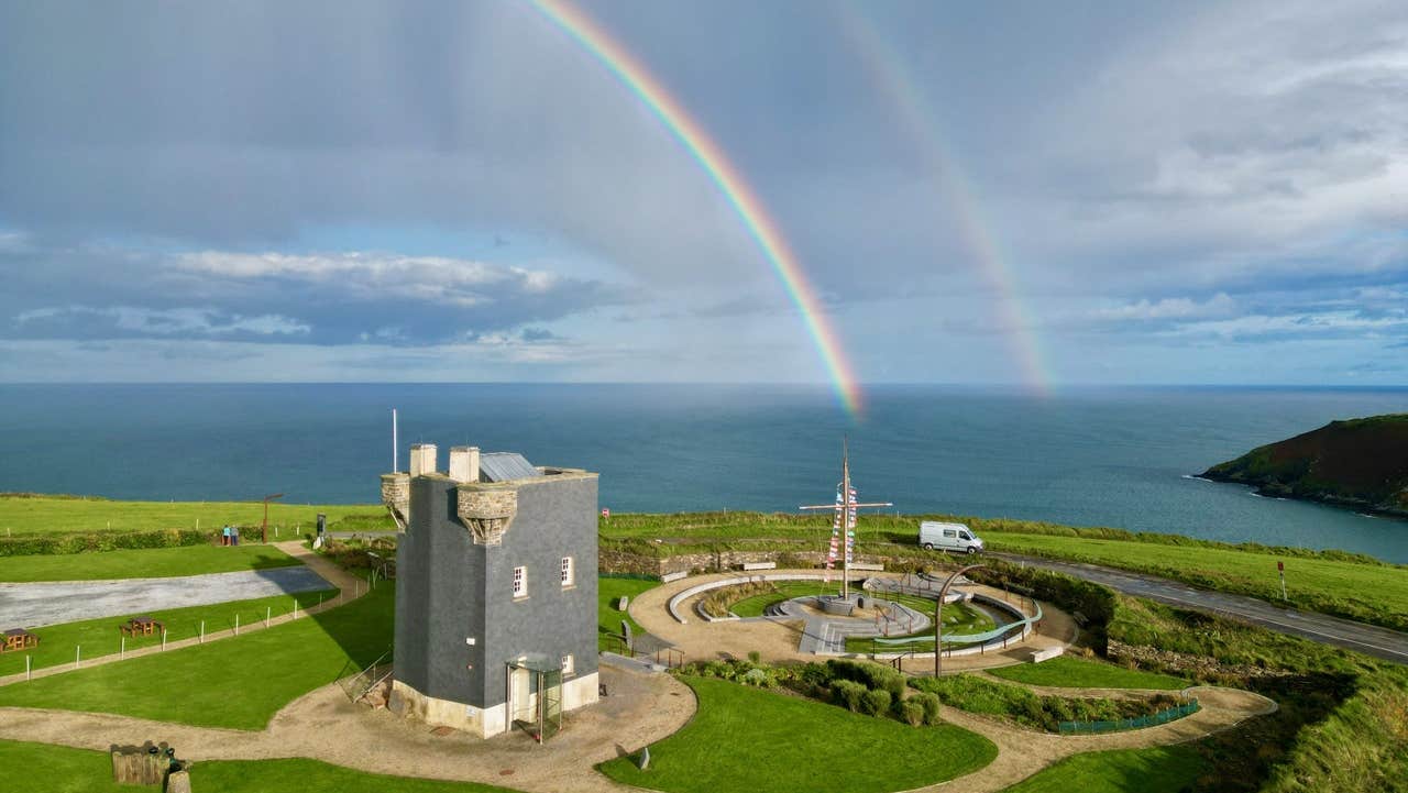A signal tower beside the coast with a double rainbow in the sky