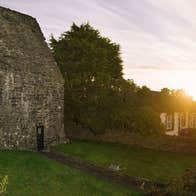 A small ancient stone building on a street lined with houses